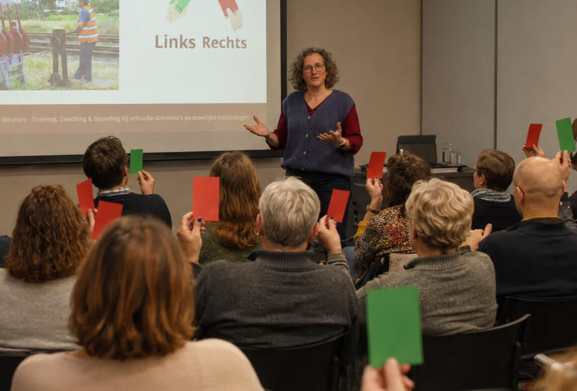 Tijdens een training aan een groep mensen legt Ils een dilemma voor waarbij de deelnemers een keuze maken met behulp van rode en groene kaarten.